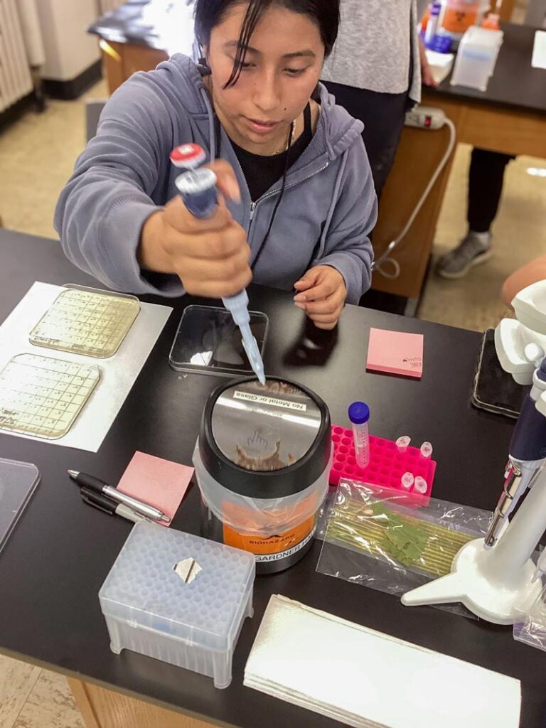 Juntos academy student learning how to use a pipette in a lab.